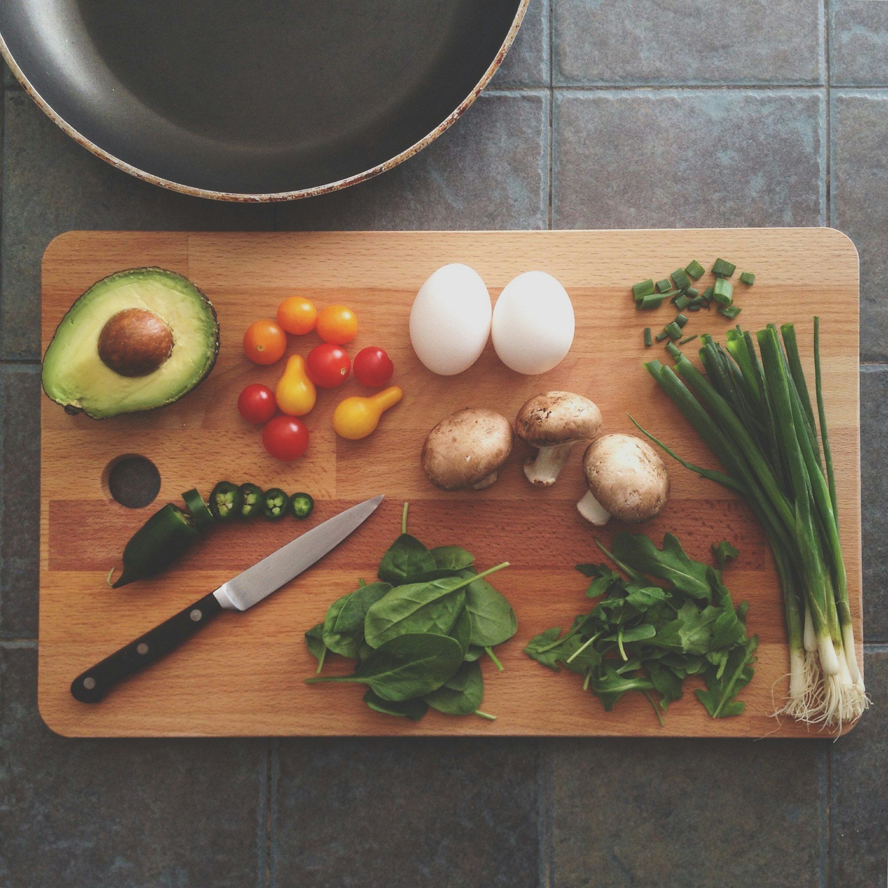 Whole-food ingredients on a wooden board: avocado, eggs, mushrooms, greens and tomatoes