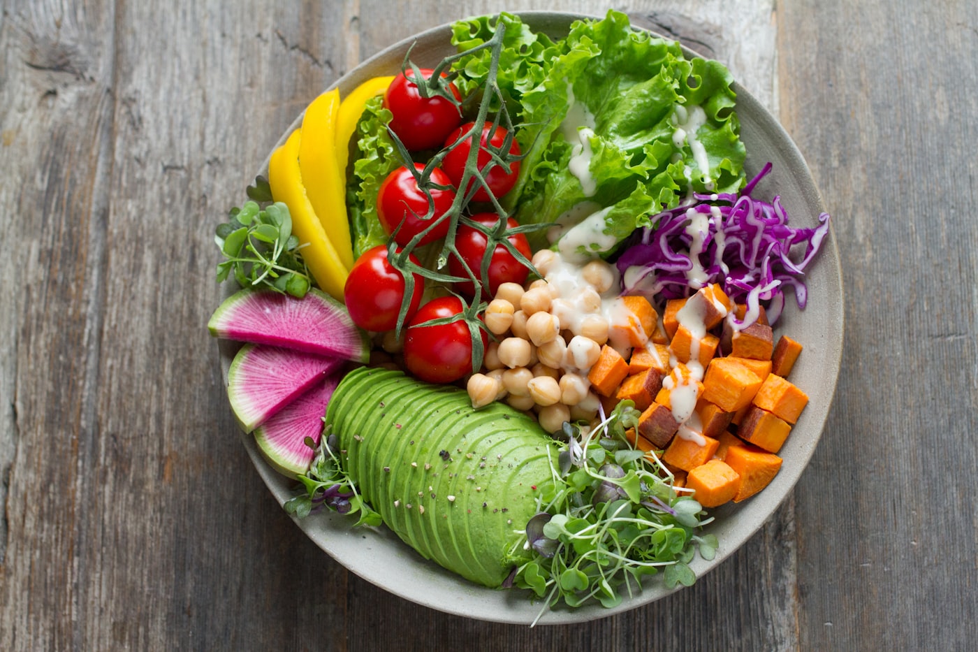 Colorful salad bowl with leafy greens, tomatoes, avocado, chickpeas and sweet potato