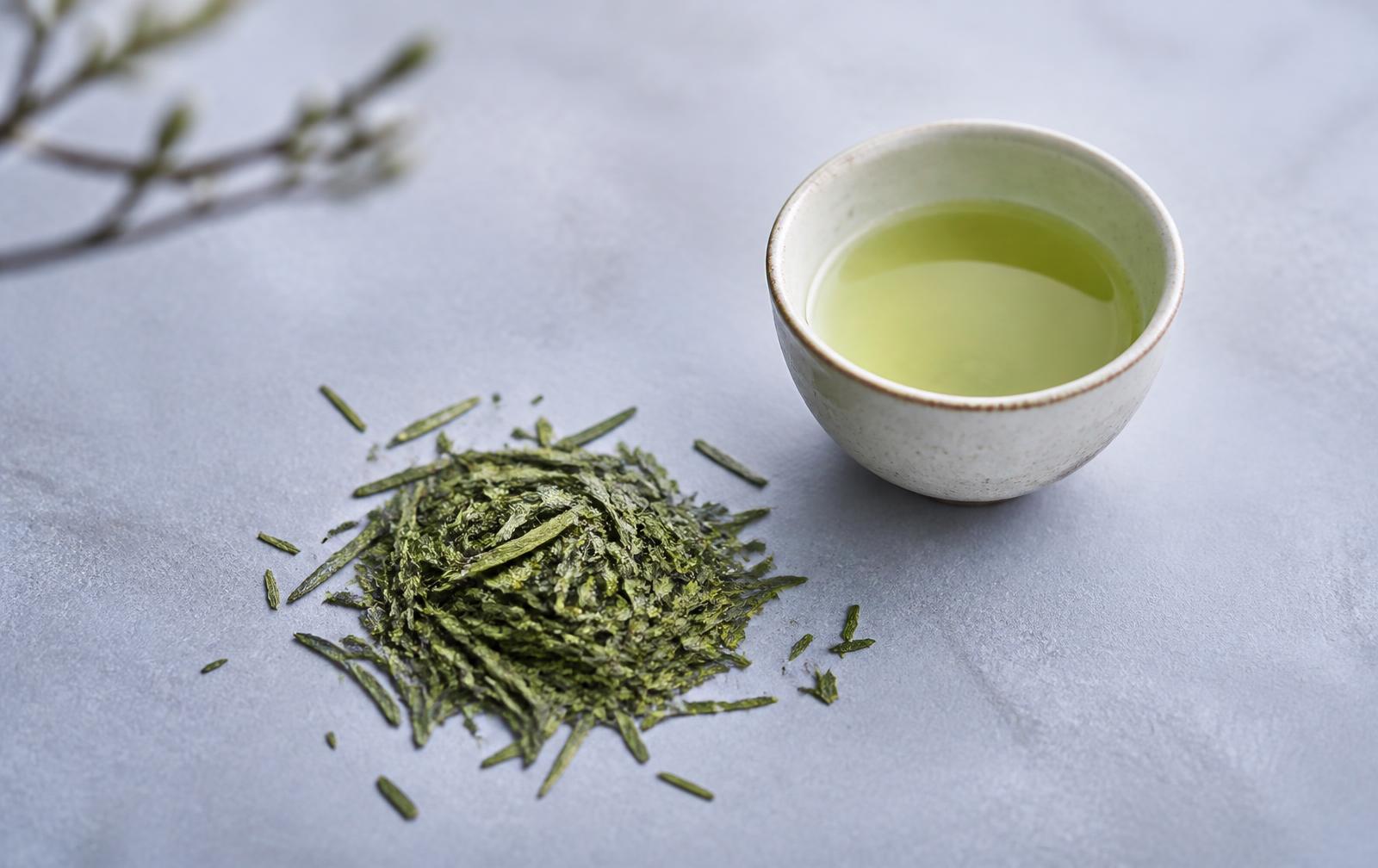 Loose green tea leaves beside a small ceramic cup of green tea