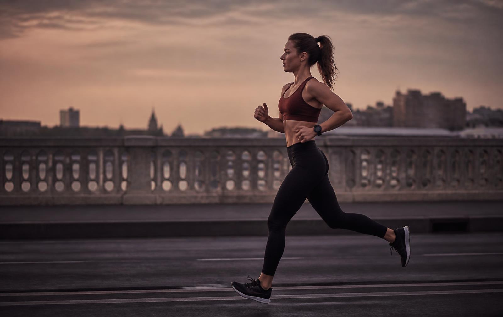 A woman running across a city bridge at dawn