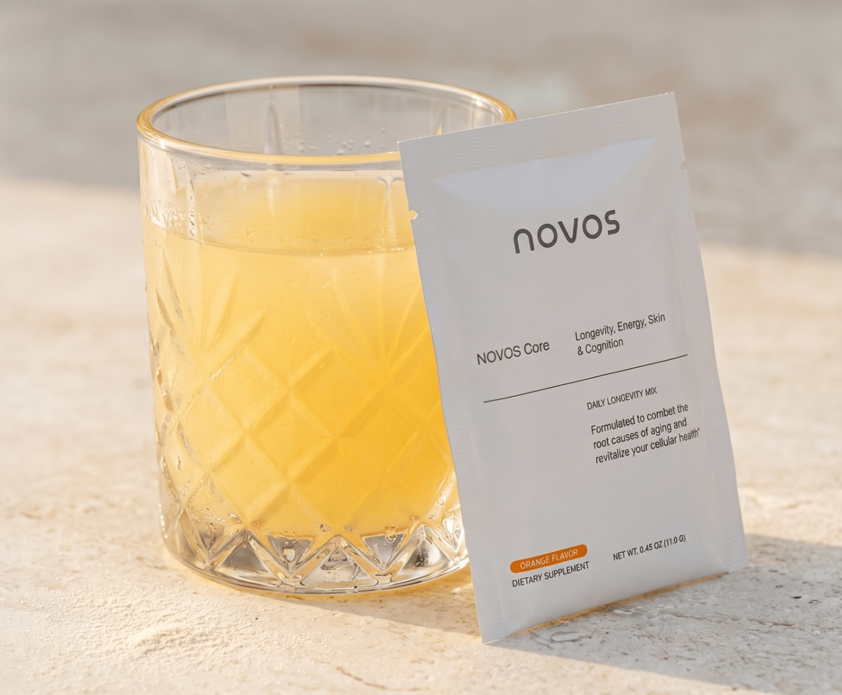 NOVOS Core sachet beside a glass of orange-flavored mix in sunlight