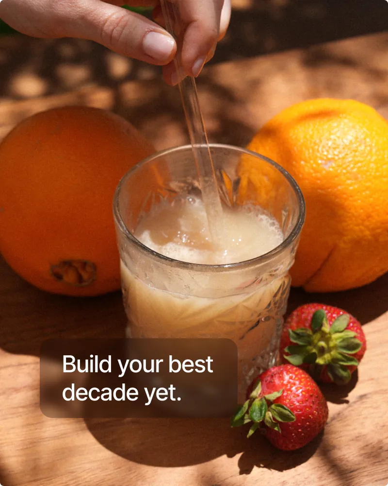 NOVOS Core stirred into a glass of water beside fresh oranges and strawberries in sunlight